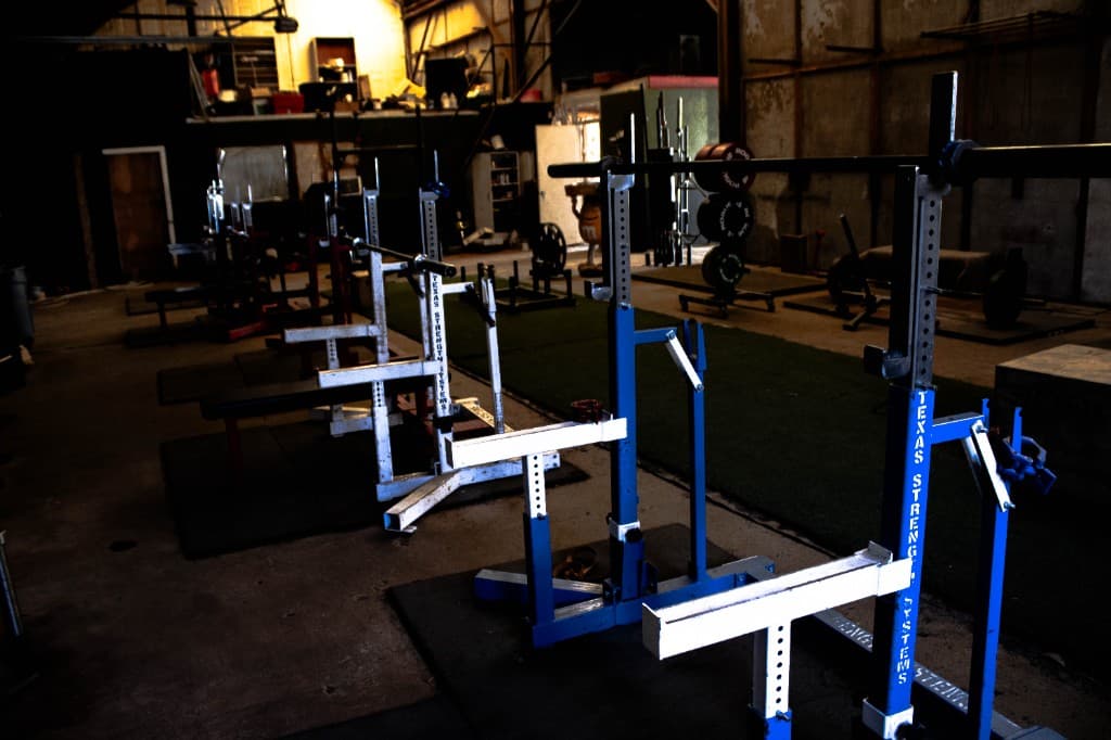 Industrial warehouse gym with professional Texas Strength Systems power racks and a turf sled track